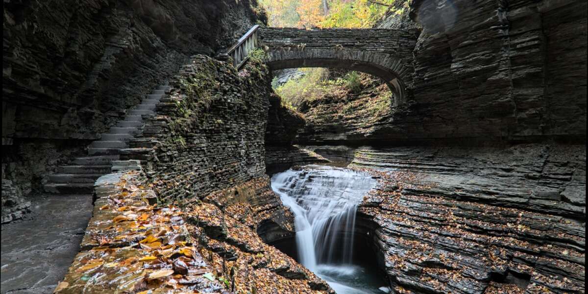 rainbow falls at watkins glen state park (waterfall in a gorge with stone bridge, staircase, glacial layered rock formation) falling water, stream, autumn colors, leaves changing, fall foliage