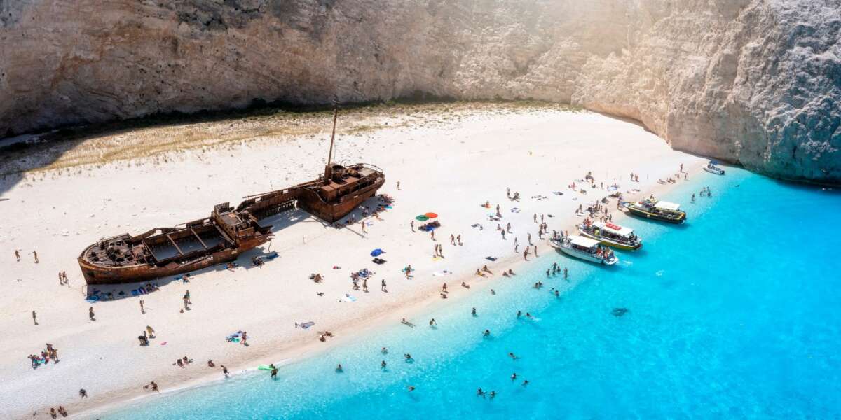 The beautiful Navagio shipwreck beach with turquoise sea and tourists enjoying the sea, Zakynthos island, Greece