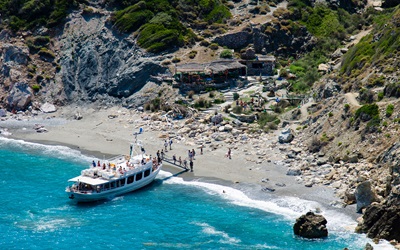 Tourist boat landing on the beach of Kastro at Skiathos on the bottom a restaurant bar and the typical island's vegetation on the cliff