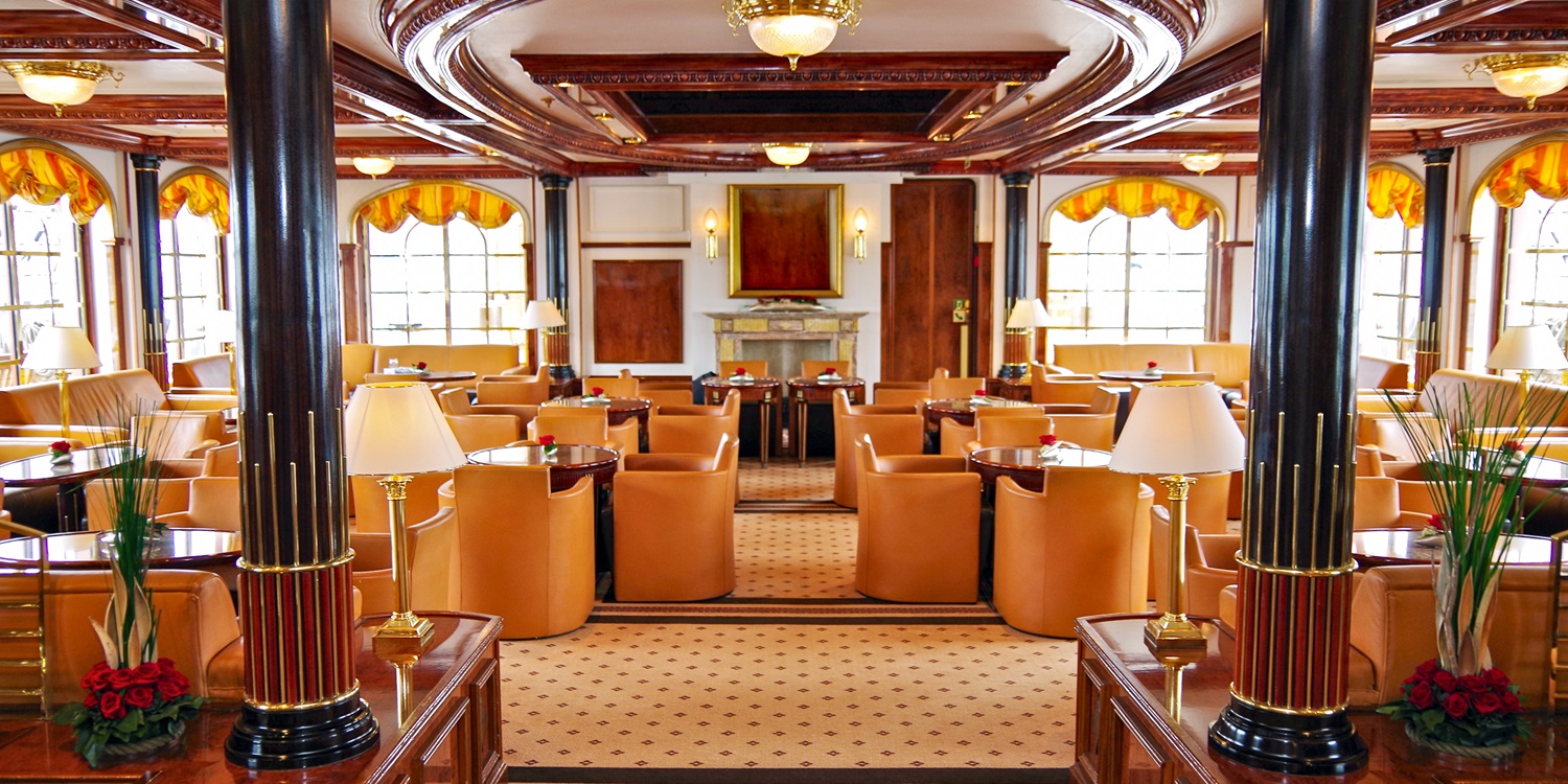 Elegante und luxuriöse Lounge Bar Aufenthaltsraum im Jugendstil auf Luxus Kreuzfahrtschiff Sea Cloud 2 mit orangenen Ledercouch und Ledersessel, Teakholz, Messing, Fenstern und Stuck Decke Intarsien