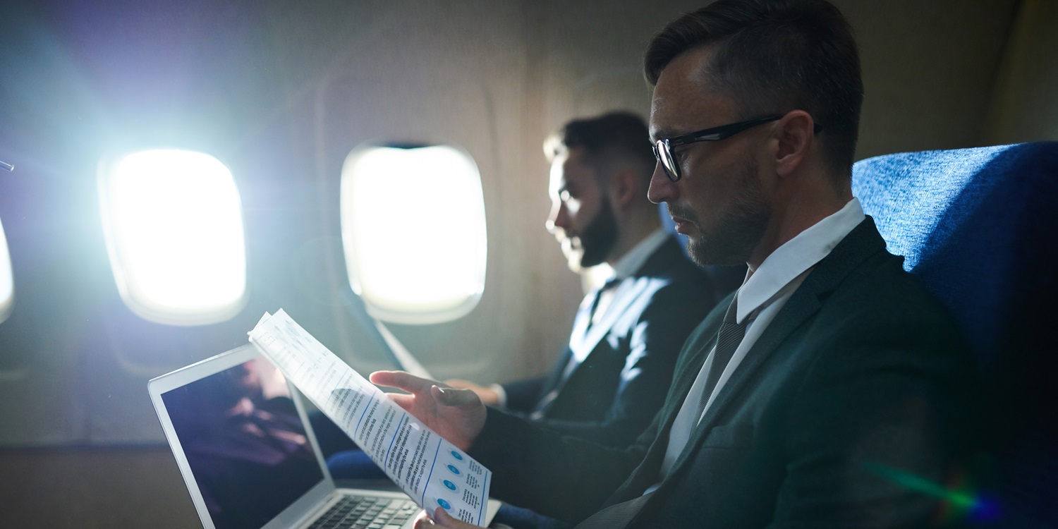 Side view portrait of two business people working and reading documents in dimly lit plane during first class flight, copy space